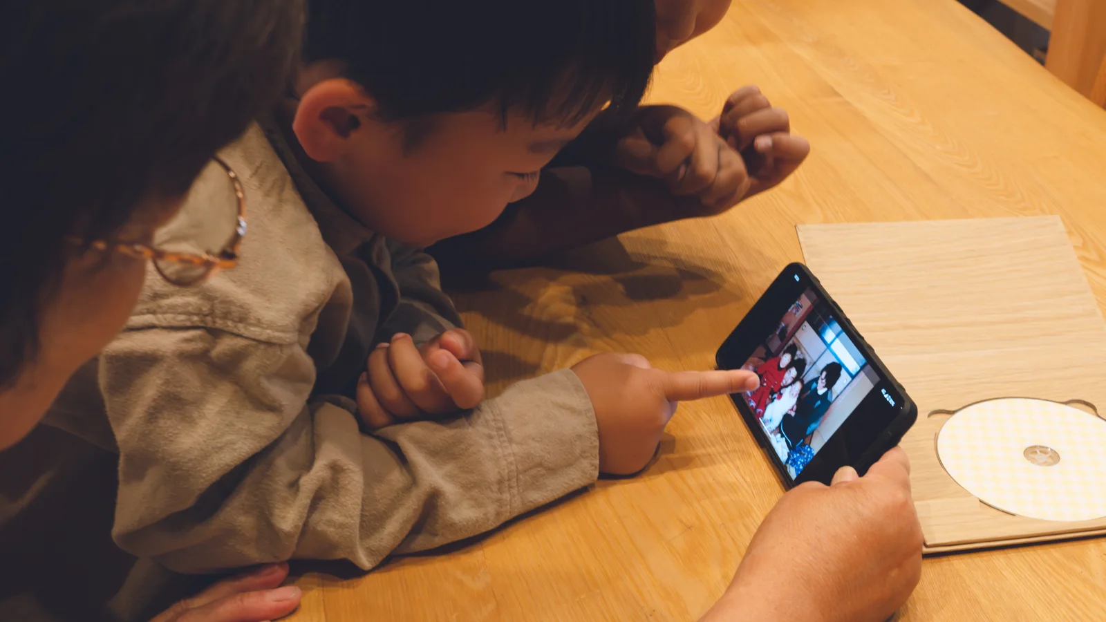 木のテーブルを囲み、家族でスマートフォンの昔の写真を見ている様子